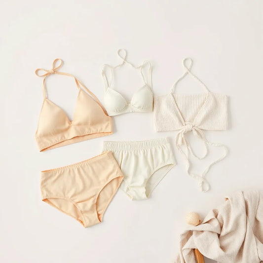 Soft bikini swimsuits in pastel tones displayed with a draped linen cover and light accessories